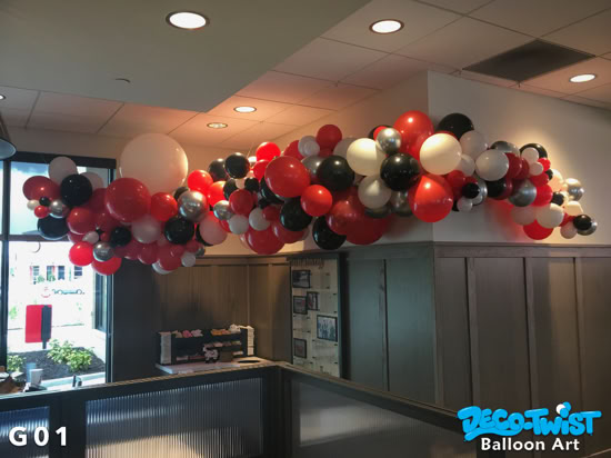 A balloon garland made of red, black, white, and silver balloons is draped along the corner of a ceiling, creating a festive and colorful decoration.