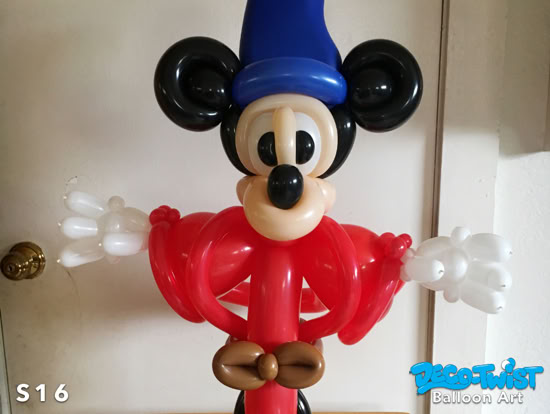 A balloon sculpture depicts a cartoon mouse character dressed as a wizard, with large round ears, a blue pointed hat, a red robe, and white gloves.