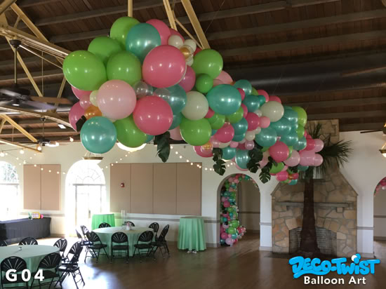 A large balloon garland made of pink, green, teal, and white balloons is suspended from the ceiling of the Magnolia Building in Lakeland, Florida adding festive color above round tables set for guests.