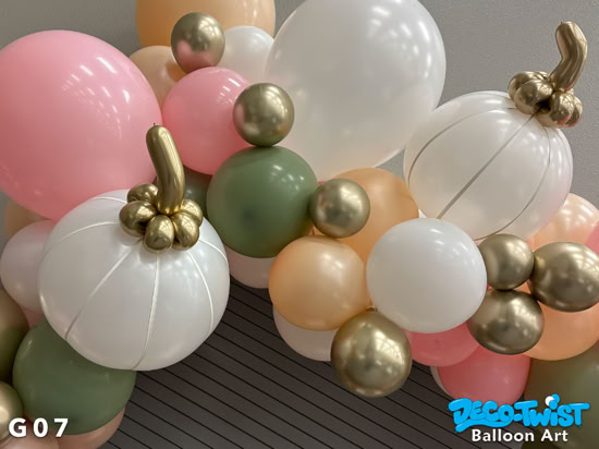 A balloon garland in soft fall colors—peach, pink, white, green, and gold—decorates a wall corner. Some balloons are shaped like pumpkins with gold stems, adding an autumn harvest theme.