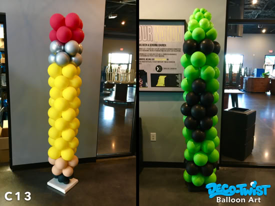 This image shows two tall balloon columns designed to look like fun, oversized objects. The column on the left resembles a pencil, with black and beige balloons at the base (for the tip), a long section of yellow balloons (the pencil body), silver balloons (the metal band), and red balloons on top (the eraser). The column on the right is made of green and black balloons arranged in alternating sections, giving it a bold striped pattern. It resembles a glowing neon theme or possibly a "creeper" character from the Minecraft game. Both columns are standing indoors as decorative pieces.